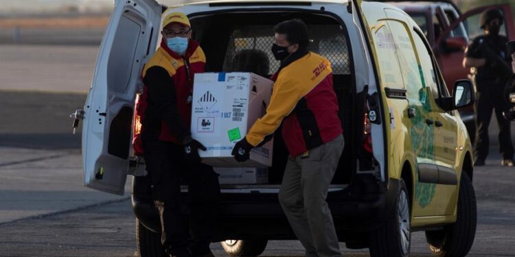Dos trabajadores de un servicio de mensajería cargaban una caja con las primeras 10.000 dosis de la vacuna contra la covid-19 en llegar a territorio chileno, el pasado 24 de diciembre. EFE/Alberto Valdés/Archivo