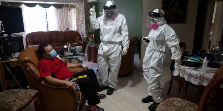 Angels of the Road volunteer paramedic Zully Rodiz, right, and Dr. Brayan Alfaro, measure the vital signs readings of a person suspected of having COVID-19, at his home in Caracas, Venezuela, Thursday, Feb. 11, 2021. The self-sufficient volunteer group, who seek their own funding and operate entirely independently of the government, are now prioritizing new coronavirus cases and offering free rides in their single ambulance to the hospital. (AP Photo/Ariana Cubillos)