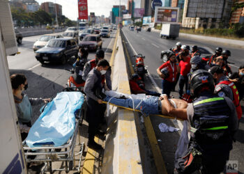 Angels of the Road volunteer paramedics move a person injured in a motorcycle accident on a scoop stretcher into their single ambulance, in Caracas, Venezuela, Wednesday, Feb. 10, 2021. The volunteer paramedics say they feed off the adrenaline of each emergency call. (AP Photo/Ariana Cubillos)