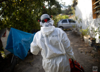 Wearing a biosecurity suit, Dr. Debora Mejia, an Angels of the Road volunteer, walks out of a house after visiting two COVID-19 patients in Caracas, Venezuela, Wednesday, Feb. 3, 2021. Each day brings on average three to four calls, and the new coronavirus pandemic means that at least one of those is a request to take a patient with trouble breathing to a hospital. (AP Photo/Ariana Cubillos)