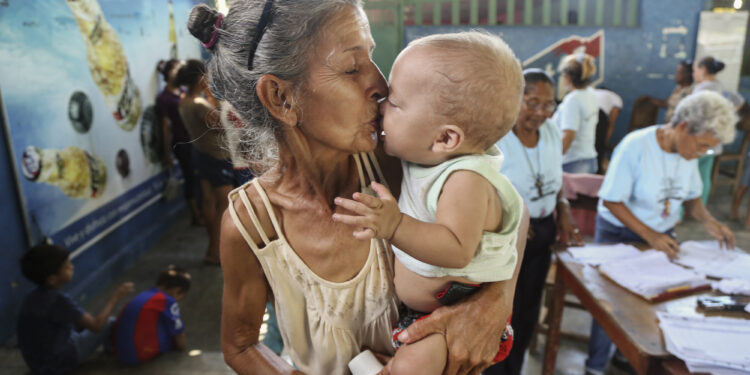 Rosa Irima, 62, gives her grandson Gabriel, a kiss during a nutrition monitoring session run by Caritas Los Teques volunteers at Club Esmeralda in Tomuso, Venezuela. Rosa is looking after four of her grandchildren. Galloping inflation has pushed 92 percent of the population into poverty. The current minimum monthly salary averages to about $1.50 and covers only 2 percent of the minimum nutritional basket. As of March 2018, it would require 73 monthly salaries solely to cover the cost of feeding a family. Families cope by selling off goods, cutting back on meals and the quantity of food served at each meal. Routine growth monitoring sessions conducted by Caritas has shown that 70 percent of children under 5 show signs of some form of nutrition with 8 percent from severe malnutrition. Galloping inflation has pushed 92 percent of the population into poverty. The current minimum monthly salary averages to about $1.50 and covers only 2 percent of the minimum nutritional basket. As of March 2018, it would require 73 monthly salaries solely to cover the cost of feeding a family. Families cope by selling off goods, cutting back on meals and the quantity of food served at each meal. Routine growth monitoring sessions conducted by Caritas has shown that 70 percent of children under 5 show signs of some form of nutrition with 8 percent from severe malnutrition.