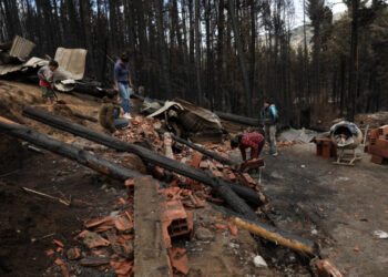 People clean rubble in Las Golondrinas town, in Chubut province, Argentina, on March 11, 2021, after a forest fire. - Seven people were injured and 15 more missing on Wednesday as forest fires ripped through Argentine Patagonia, official sources said. Some 200 people had to be evacuated and around 100 homes were damaged by fire in an area of forests and lakes popular with tourists close to the Andes mountain range. (Photo by FRM / AFP)