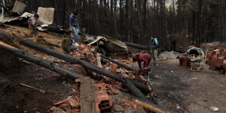 People clean rubble in Las Golondrinas town, in Chubut province, Argentina, on March 11, 2021, after a forest fire. - Seven people were injured and 15 more missing on Wednesday as forest fires ripped through Argentine Patagonia, official sources said. Some 200 people had to be evacuated and around 100 homes were damaged by fire in an area of forests and lakes popular with tourists close to the Andes mountain range. (Photo by FRM / AFP)