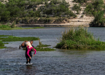 An asylum-seeking migrant man from Venezuela carries an elderly woman as he walks in the water to cross the Rio Grande river into the United States from Mexico in Del Rio, Texas, U.S., May 26, 2021. REUTERS/Go Nakamura