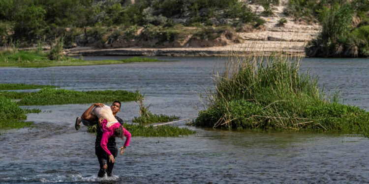 An asylum-seeking migrant man from Venezuela carries an elderly woman as he walks in the water to cross the Rio Grande river into the United States from Mexico in Del Rio, Texas, U.S., May 26, 2021. REUTERS/Go Nakamura
