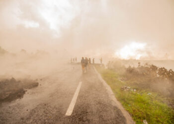 Residents walk through the smoke from smouldering lava flewing from Mount Nyiragongo in Goma on May 23, 2021. - A river of boiling lava came to a halt on the outskirts of Goma Sunday, sparing the city in eastern DR Congo from disaster after the nighttime eruption of Mount Nyiragongo sent thousands of terrified residents fleeing in panic.
Fire and strong fumes emanated from the blackish molten rock as it swallowed up houses, heading towards Goma airport on the shores of Lake Kivu. (Photo by Moses Sawasawa / AFP)