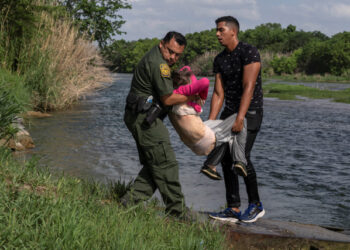 An U.S. Border Patrol agent and an asylum-seeking migrant man carry an elderly migrant woman from Venezuela after crossing the Rio Grande river into the United States from Mexico in Del Rio, Texas, U.S., May 26, 2021. REUTERS/Go Nakamura