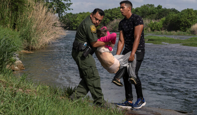 An U.S. Border Patrol agent and an asylum-seeking migrant man carry an elderly migrant woman from Venezuela after crossing the Rio Grande river into the United States from Mexico in Del Rio, Texas, U.S., May 26, 2021. REUTERS/Go Nakamura