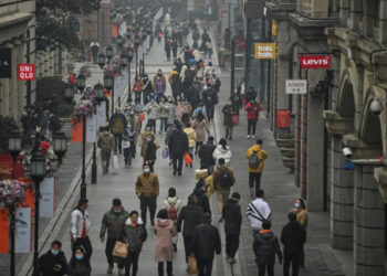 People walk along a pedestrian street in Wuhan, China's central Hubei province on January 23, 2021, one year after the city went into lockdown to curb the spread of the Covid-19 coronavirus. (Photo by Hector RETAMAL / AFP)
