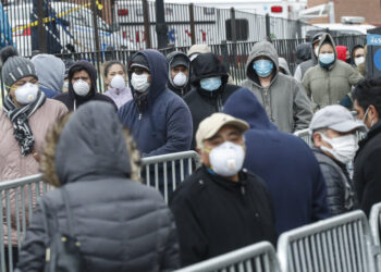 Patients wear personal protective equipment while maintaining social distancing as they wait in line for a COVID-19 test at Elmhurst Hospital Center, Wednesday, March 25, 2020, in New York. Gov. Andrew Cuomo sounded his most dire warning yet about the coronavirus pandemic Tuesday, saying the infection rate in New York is accelerating and the state could be as close as two weeks away from a crisis that sees 40,000 people in intensive care. Such a surge would overwhelm hospitals, which now have just 3,000 intensive care unit beds statewide. (AP Photo/John Minchillo)