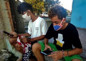 Boys wearing face masks with the US flag connect to internet in a street of Havana, on April 13, 2021. - Cuba's Communist Party congress will meet for four days starting Friday, marking the departure of Raul Castro in a country shaken by the economic crisis and the recent arrival of mobile internet. (Photo by YAMIL LAGE / AFP)