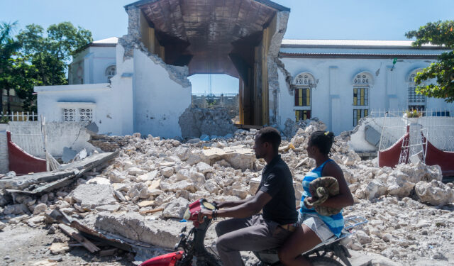 People drive past the remains of the "Sacré coeur des Cayes" church in Les Cayes on August 15, 2021, after a 7.2-magnitude earthquake struck the southwest peninsula of the country. - Hunched on benches, curled up in chairs or even lying the floor, those injured in the powerful earthquake that wreaked havoc on Haiti on Saturday crowded an overburdened hospital near the epicenter. The emergency room in Les Cayes, in southwestern Haiti, which was devastated by the 7.2-magnitude quake on Saturday morning that killed at least 724 people, is expecting reinforcements to help treat some of the thousands of injured. (Photo by Reginald LOUISSAINT JR / AFP)