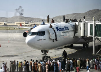 Afghan people climb atop a plane as they wait at the Kabul airport in Kabul on August 16, 2021, after a stunningly swift end to Afghanistan's 20-year war, as thousands of people mobbed the city's airport trying to flee the group's feared hardline brand of Islamist rule. (Photo by Wakil Kohsar / AFP)