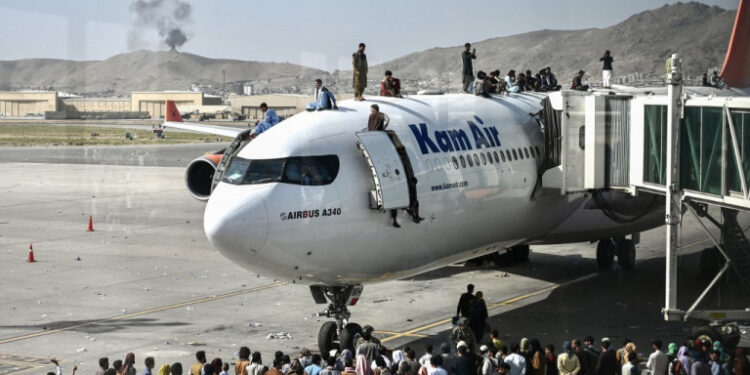 Afghan people climb atop a plane as they wait at the Kabul airport in Kabul on August 16, 2021, after a stunningly swift end to Afghanistan's 20-year war, as thousands of people mobbed the city's airport trying to flee the group's feared hardline brand of Islamist rule. (Photo by Wakil Kohsar / AFP)