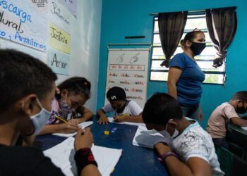 Niños hacen tareas en sus cuadernos durante una clase en la casa de la maestra Jasmín Castro, el 20 de agosto de 2021, en Petare, Caracas (Venezuela). Maestras preocupadas por la educación de los niños que habitan en Petare, una de las barriadas más pobres de Venezuela, abrieron las puertas de sus casas para educar a los chicos en medio del cierre de escuelas, empujado por la covid-19, que ya suma más de un año y el difícil acceso a internet. EFE/ RAYNER PEÑA R.
