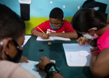 Niños hacen tareas en sus cuadernos durante una clase en la casa de la maestra Jasmín Castro, el 20 de agosto de 2021, en Petare, Caracas (Venezuela). Maestras preocupadas por la educación de los niños que habitan en Petare, una de las barriadas más pobres de Venezuela, abrieron las puertas de sus casas para educar a los chicos en medio del cierre de escuelas, empujado por la covid-19, que ya suma más de un año y el difícil acceso a internet. EFE/ RAYNER PEÑA R.
