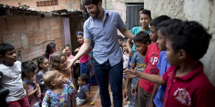 En esta imagen, tomada el 26 de agosto de 2018, Roberto Patiño saluda a niños en un centro infantil en el vecindario de La Vega, en Caracas, Venezuela. Patiño, una estrella al alza en el movimiento opositor en Venezuela, y otros organizadores de base que tienen entre 20 y 30 años han estado dando de comer a los niños, animando a las mujeres a convertirse en activistas por su comunidad y organizando protestas para exigir servicios públicos como agua potable y electricidad. (AP Foto/Ariana Cubillos)