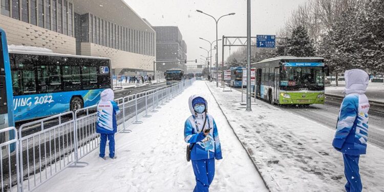 Voluntarios olímpicos se paran en una estación de autobuses frente al centro de medios olímpico, que forma parte de la 'burbuja' olímpica COVID-19, en un día nevado, durante los Juegos Olímpicos de Pekín 2022 en Pekín, China. EFE/EPA/PILIPEY ROMANA