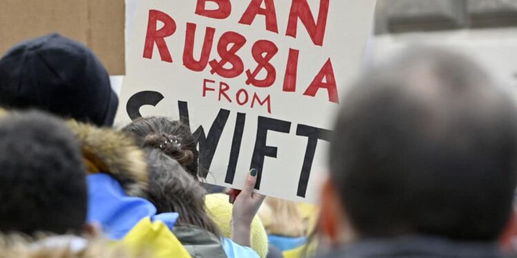 A demonstrator holds a poster reading "Ban Russia from SWIFT" during a protest against Russia's invasion of Ukraine, on February 26, 2022 in front of the Russian embassy in Vienna, Austria. - Austria OUT (Photo by HANS PUNZ / APA / AFP) / Austria OUT (Photo by HANS PUNZ/APA/AFP via Getty Images)