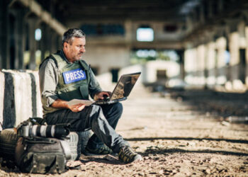 One man, war journalist with using laptop at the place of action, in war zone.