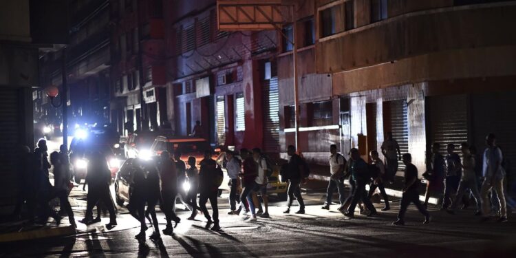 People cross a street during a power cut in Caracas on March 7, 2019. - The government of Nicolas Maduro denounced a "sabotage" against the main electric power dam in the country, after a massive blackout left Caracas and vast regions of Venezuela in the darkness. (Photo by YURI CORTEZ / AFP)
