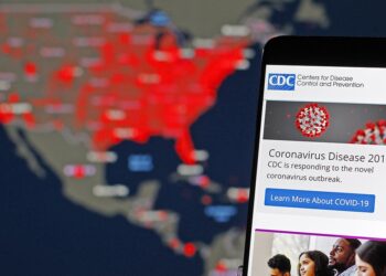 Página web de los CDC desplegada en un teléfono móvil y al fondo un mapa