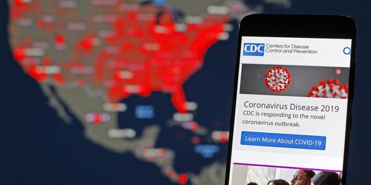Página web de los CDC desplegada en un teléfono móvil y al fondo un mapa