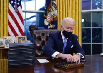 President Joe Biden reaches for a pen to sign his first executive order in the Oval Office of the White House on Wednesday, Jan. 20, 2021, in Washington. (AP Photo/Evan Vucci)
