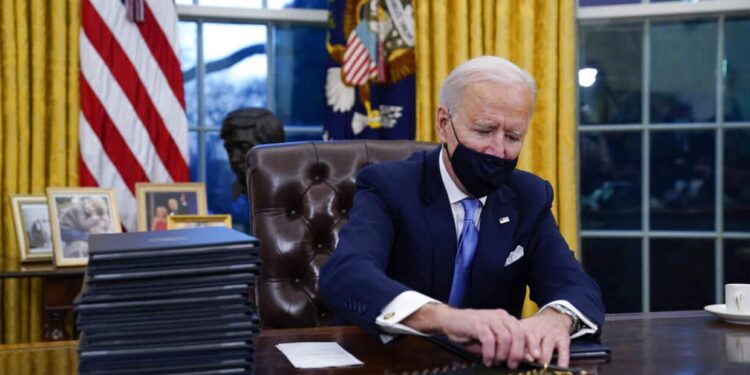 President Joe Biden reaches for a pen to sign his first executive order in the Oval Office of the White House on Wednesday, Jan. 20, 2021, in Washington. (AP Photo/Evan Vucci)