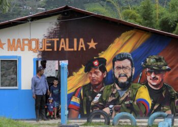 (FILES) In this file photo taken on October 27, 2021, a man and children stand next to a graffitis of late FARC commander Alfonso Cano (C) at El Oso Territorial Training and Reincorporation Area (ETCR), in Gaitania, Tolima Department, Colombia. - The US government has notified Congress that it will remove the official terror group designation from former rebels of the Revolutionary Armed Forces of Colombia (FARC), a congressional source told AFP on November 23, 2021. (Photo by Raul ARBOLEDA / AFP)