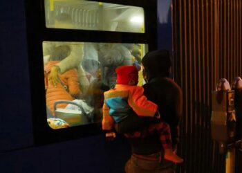 Migrantes, en su mayoría venezolanos, se refugian del frío en un autobús de transporte público durante una noche de bajas temperaturas, mientras otro migrante con su hijo los observa desde afuera, en el centro de El Paso, Texas, EE. UU., el 23 de diciembre , 2022. REUTERS/José Luis González