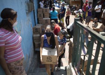 Una mujer que porta una mascarilla para protegerse del coronavirus carga una caja con alimentos básicos proporcionada por un programa de asistencia alimentaria del gobierno, en el barrio pobre de Petare en Caracas, Venezuela, el jueves 30 de abril de 2020. (AP Foto/Ariana Cubillos)