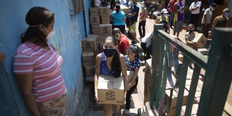Una mujer que porta una mascarilla para protegerse del coronavirus carga una caja con alimentos básicos proporcionada por un programa de asistencia alimentaria del gobierno, en el barrio pobre de Petare en Caracas, Venezuela, el jueves 30 de abril de 2020. (AP Foto/Ariana Cubillos)