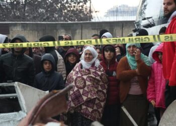 Víctimas del terremoto se juntan tras una cinta policial mientras ven el desastre que quedó en Diyarbakir, Turquía.