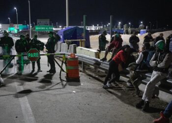 Migrantes permanecen a un lado de la vía mientras esperan soluciones a su situación migratoria, el 3 de mayo de 2023, en el paso fronterizo Chacalluta, en Arica (Chile). Jimir, Yuri y Belquis jamás se vieron aunque estuvieron en sitios parecidos, jamás hablaron, pero si lo hubieran hecho en la penúltima parada que les deparó su azarosa vida de migrantes, huyendo de Chile, se habrían sorprendido de qué parejos eran sus sueños rotos, sus miedos, su destino compartido. EFE/ Lucas Aguayo Araos