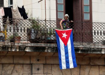 Una mujer sale al balcón donde se expone una bandera cubana, en La Habana, Cuba. EFE/Ernesto Mastrascusa/Archivo