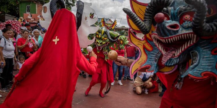 Un grupo de promeseros bailan con máscaras durante la celebración religiosa de los Diablos Danzantes de Yare hoy, en San Francisco de Yare, estado Miranda (Venezuela). Cientos de creyentes marcharon este jueves en Venezuela en una procesión centenaria, conocida como los "Diablos Danzantes de Yare", con la que penitentes vestidos de rojo y con el rostro cubierto con máscaras estrafalarias celebran el triunfo del bien sobre el mal en el marco de la festividad católica del Corpus Christi. EFE/ Rayner Peña R.