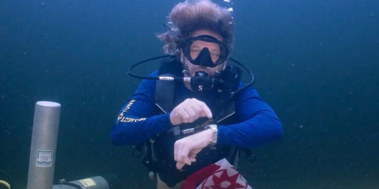 En esta fotografía facilitada por la Oficina de Prensa de los Cayos de Florida, el explorador submarino e investigador médico, doctor Joseph Dituri, señala su reloj para indicar que llegó la hora de volver a la superficie tras pasar 100 días (nuevo récord) en el refugio submarino Jules' Undersea Lodge, situado en el fondo de una laguna de Key Largo, en Florida (AP)