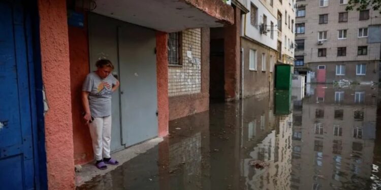 Una mujer se para junto a la entrada de su casa en una calle inundada, tras la rotura de la presa de Nova Kakhovka en Jersón, Ucrania, el 6 de junio. (Crédito: Alina Smutko/Reuters)