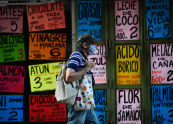 A man walks past signs displaying prices of products in US dollars outside a supermarket in Caracas on December 9, 2020. - In Venezuelan nobody wants bolivars, the weakened national currency. Everything can be payed for in dollars, which have been prohibited for 15 years, but keep gaining power in a country hit by years of recession and hyperinflation. (Photo by Federico PARRA / AFP) (Photo by FEDERICO PARRA/AFP via Getty Images)