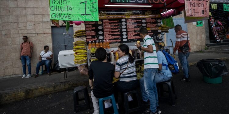 ACOMPAÑA CRÓNICA: VENEZUELA JUVENTUD***AME9877. CARACAS (VENEZUELA), 11/08/2023.- Jóvenes se alimentan en un local de comida callejera, el 3 de agosto de 2023 en Caracas (Venezuela). Las jóvenes venezolanas Ysleydi González y Catherine Porciello, pese a sus marcadas diferencias económicas, comparten una misma preocupación: ven como una utopía generar un patrimonio con recursos propios en su país, donde se necesita trabajar más de 41 años para comprar un apartamento de una habitación en una modesta zona de Caracas, con un costo de unos 25.000 dólares. EFE/MIGUEL GUTIÉRREZ