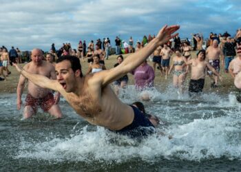 Revelers take part in the annual L-Street Brownies cold water plunge at M Street beach on New Years Day, January 1, 2024 in Boston, Massachusetts. The plunge on New Year's day dates back over 100 years in Boston. Monies from T-shirt sales are to be given to local charities.  The National Oceanic and Atmospheric Administration (NOAA) reported the water temp in Boston Harbor to be at 44.6F (7C) and air was measured at 30F (-1C). (Photo by Joseph Prezioso / AFP)