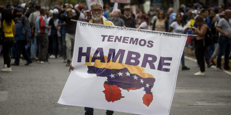 AME082. CARACAS (VENEZUELA), 15/01/2024.- Un hombre sostiene un cartel de protesta durante una manifestación de maestros, respaldados por trabajadores de otros sectores, contra los bajos salarios y para exigir mejoras laborales, hoy, en Caracas (Venezuela). Cientos de maestros en Venezuela volvieron a las calles este lunes, cuando se conmemora su día en el país, con el objetivo de exigir al Gobierno de Nicolás Maduro la reanudación de las negociaciones para una nueva convención colectiva. Esta es la segunda jornada de manifestaciones de trabajadores de este año, que comenzaron el pasado 9 de enero. EFE/ Miguel Gutiérrez