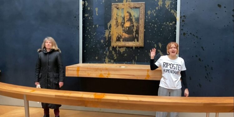 This image grab taken from AFPTV footage shows two environmental activists from the collective dubbed "Riposte Alimentaire" (Food Retaliation) gesturing as they stand in front of Leonardo Da Vinci's "Mona Lisa" (La Joconde) painting after hurling soup at the artwork, at the Louvre museum in Paris, on January 28, 2024. Two protesters on January 28, 2024 hurled soup at the bullet-proof glass protecting Leonardo da Vinci's "Mona Lisa" in Paris, demanding the right to "healthy and sustainable food", an AFP journalist said. It is the latest attack on the masterpiece in the French capital's Louvre museum, after someone threw a custard pie at it in May 2022, but it's thick glass casing ensured it came to no harm. (Photo by David CANTINIAUX / AFPTV / AFP)