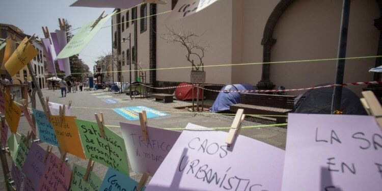 A picture taken in La Laguna on the Spanish Canary island of Tenerife, on April 13, 2024 shows signs written by protesters next to tents of activists on hunger strike to protest against mass tourism infrastructures. Activists started hunger strike on April 11 to demand a moratorium on mass tourism on the Canary Islands. (Photo by DESIREE MARTIN / AFP)