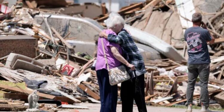 Dos mujeres se abrazan frente a sus casas, destrozadas por un tornado en Greenfield, Iowa. (AP FotoCharlie Neibergall).