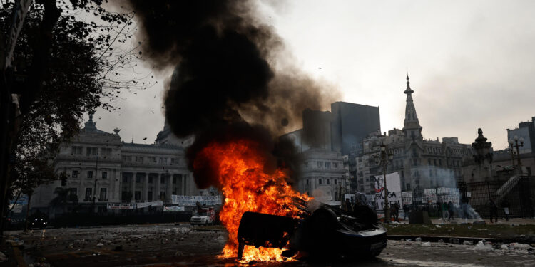 AME3687. BUENOS AIRES (ARGENTINA), 12/06/2024.- Fotografía de un auto quemado durante enfrentamientos entre la policía y personas que protestan a las afueras del senado durante un debate este miércoles, en Buenos Aires (Argentina). Manifestantes y policías protagonizan un choque este miércoles a las puertas del Senado de Argentina mientras la cámara legislativa debate la ley de Bases, el proyecto estrella del Gobierno, con el que el presidente Javier Milei pretende implementar un paquete de reformas económicas de gran calado. EFE/ Juan Ignacio Roncoroni