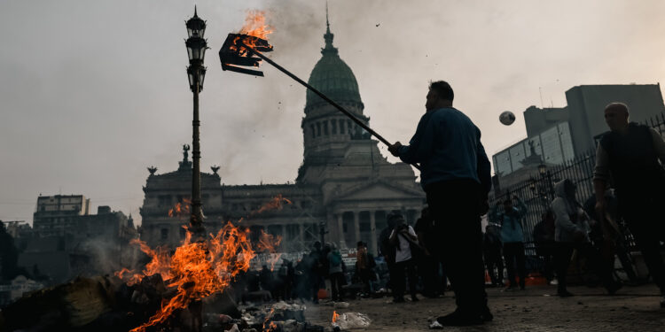 AME3498. BUENOS AIRES (ARGENTINA), 12/06/2024.- Un hombre quema una caja durante enfrentamientos entre la policía y personas que protestan a las afueras del senado durante un debate este miércoles, en Buenos Aires (Argentina). Manifestantes y policías protagonizan un choque este miércoles a las puertas del Senado de Argentina mientras la cámara legislativa debate la ley de Bases, el proyecto estrella del Gobierno, con el que el presidente Javier Milei pretende implementar un paquete de reformas económicas de gran calado. EFE/ Juan Ignacio Roncoroni