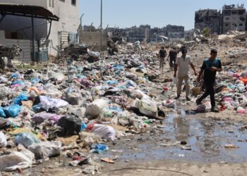 Palestinian man walk past mounds of garbage and open sewage in the Sheikh Radwan neighbourhood, north of Gaza City, on July 3, 2024, amid the ongoing conflict between Israel and the militant Hamas group. - Israel's military said on July 3, it was conducting raids backed by air strikes in northern Gaza, killing "dozens" of militants in an area where it had declared the command structure of Hamas dismantled months ago. (Photo by Omar AL-QATTAA / AFP)