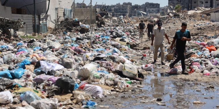 Palestinian man walk past mounds of garbage and open sewage in the Sheikh Radwan neighbourhood, north of Gaza City, on July 3, 2024, amid the ongoing conflict between Israel and the militant Hamas group. - Israel's military said on July 3, it was conducting raids backed by air strikes in northern Gaza, killing "dozens" of militants in an area where it had declared the command structure of Hamas dismantled months ago. (Photo by Omar AL-QATTAA / AFP)